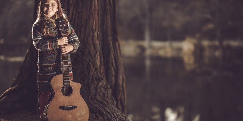 Girl With Guitar in the Park. Little Caucasian Girl with Acoustic Guitar in Hands. Young Guitarist.