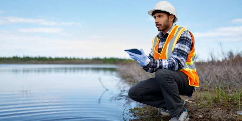 Portait of a professional scientist with protective gear examining the marsh lands in Canada and taking sample reading on a digital tablet